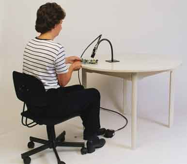 Operator seated at a workbench using a hands-free blow-off gun over a circuit board